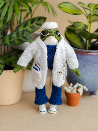 Knitted frog character in a lab coat with plants in the background