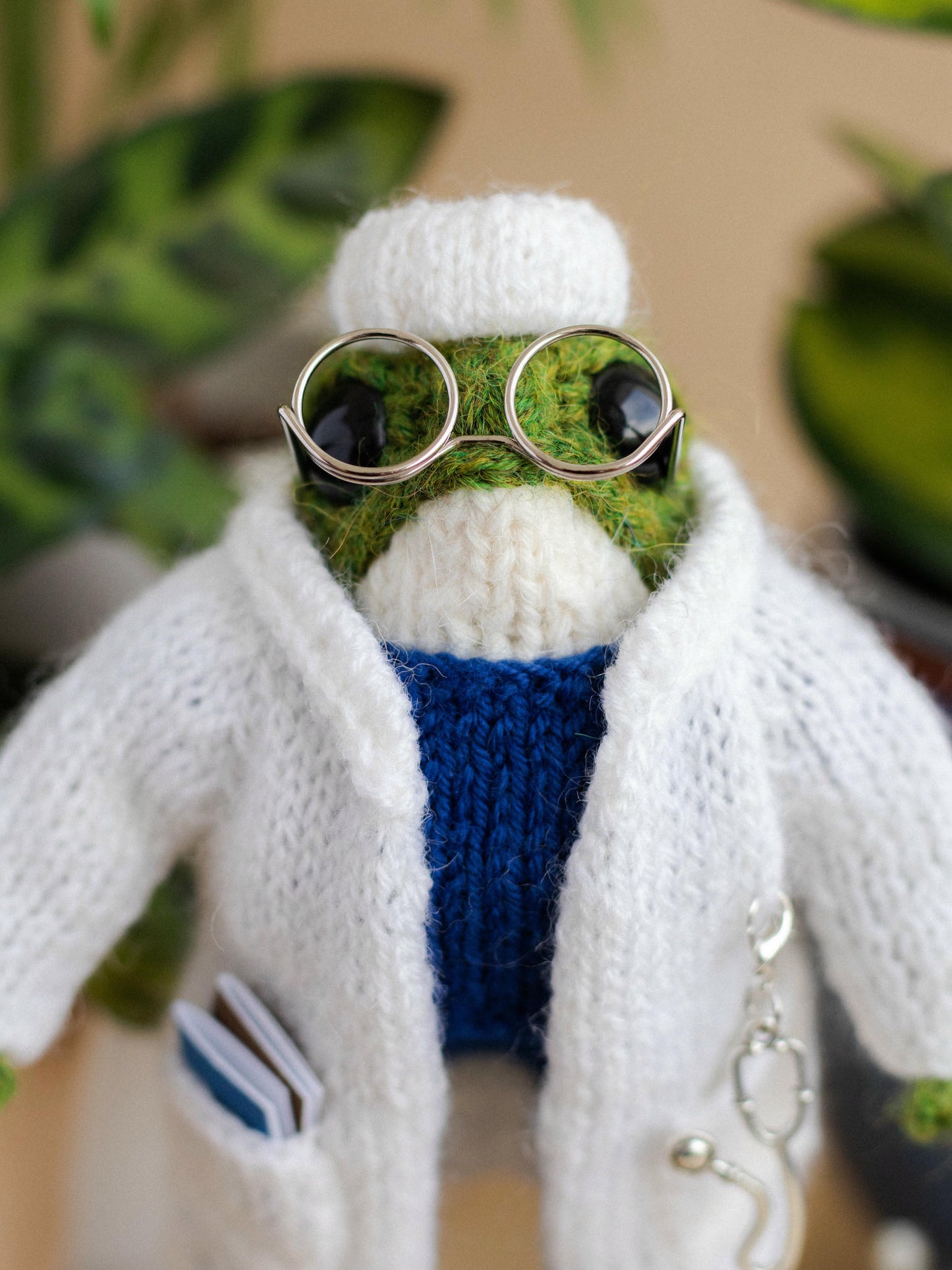 Knitted toy resembling a doctor with a white coat, green head, and blue vest.