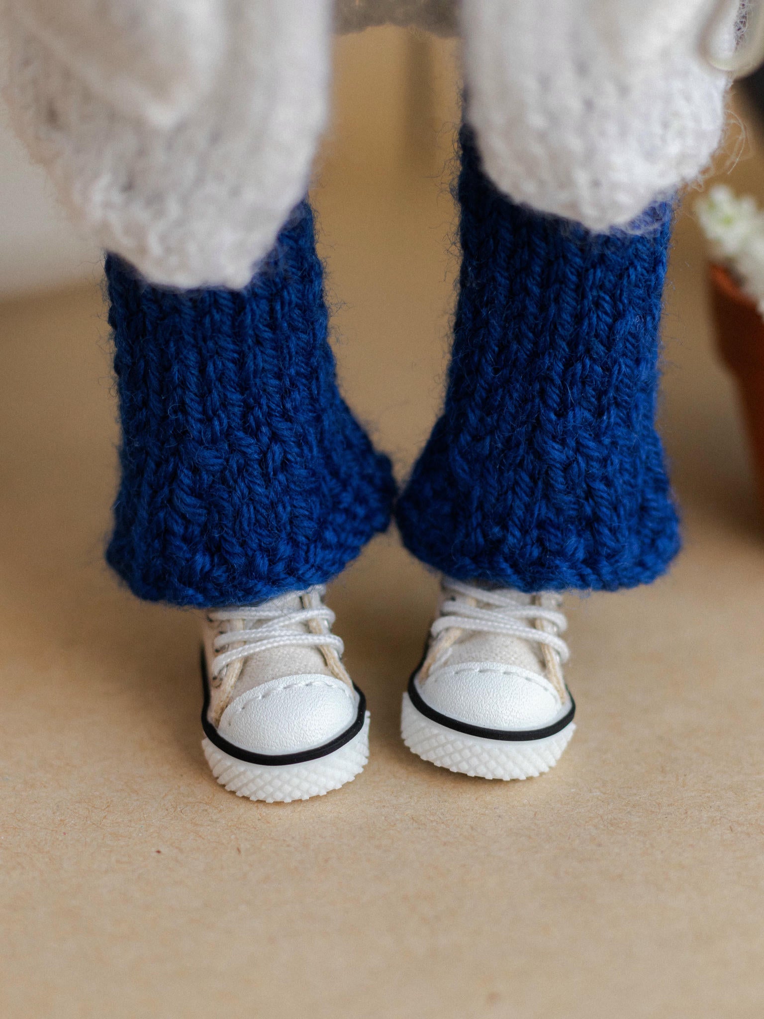 Close-up of a person wearing blue knitted leggings and white sneakers on a beige surface.