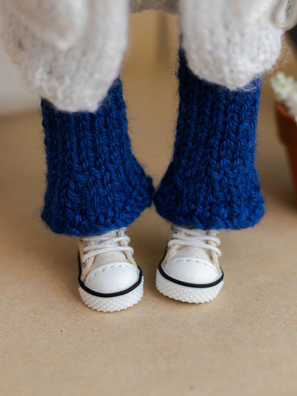 Close-up of a person wearing blue knitted leggings and white sneakers on a beige surface.