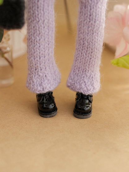 Close-up of doll legs wearing purple knitted leggings and black shoes on a beige surface.